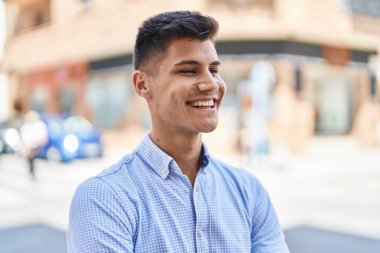 Young hispanic man smiling confident looking to the side at street