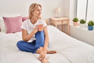 Genç sarışın kadın yatakta bir fincan kahve içiyor.
