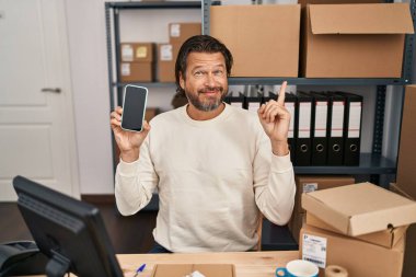 Küçük işletme şirketinde çalışan yakışıklı orta yaşlı bir adam elinde akıllı bir telefonla mutlu bir şekilde elini ve parmağını kenarda gezdiriyor. 