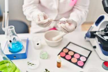 Young hispanic woman wearing scientist uniform mixing powder at laboratory