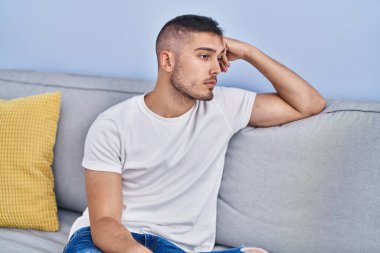 Young hispanic man stressed sitting on sofa at home