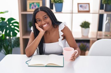 African american woman drinking coffee reading book at home