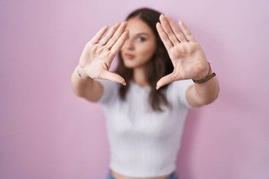 Pembe arka planda duran genç İspanyol kız el ve parmaklarıyla çerçeve yapıyor, kamera bakış açısı. 