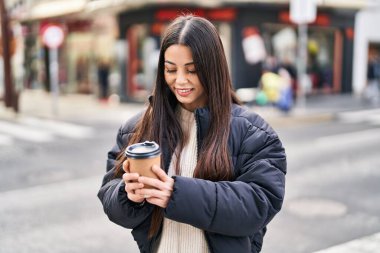Young beautiful hispanic woman smiling confident drinking coffee at street