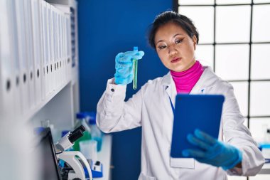 Young chinese woman scientist holding test tube having video call at laboratory