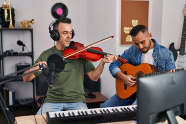 Müzik stüdyosunda klasik gitar ve keman çalan iki adam.