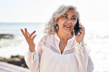 Orta yaşlı bir kadın deniz kenarında akıllı telefondan konuşarak kendine güveniyor.