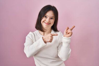 Pembe arka planda duran, gülümseyen ve kameraya bakan, iki eli ve parmağı yanda olan kadın sendromu.. 