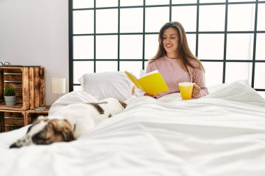 Genç bir kadın kitap okuyor ve kanepede köpeğiyle oturup kahve içiyor.