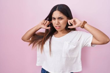 Pembe arka planda duran genç Arap kadın yüksek sesli müziğin gürültüsü için parmaklarıyla kulaklarını kapatıyor. sağır kavramı. 