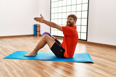 Genç kızıl saçlı, gülümseyen, kendine güvenen bir adam spor merkezinde formda top kullanıyor.