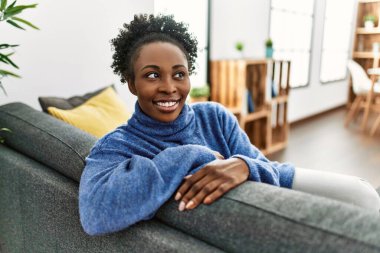 Afro-amerikalı bir kadın evdeki koltukta kendinden emin bir şekilde oturuyor.