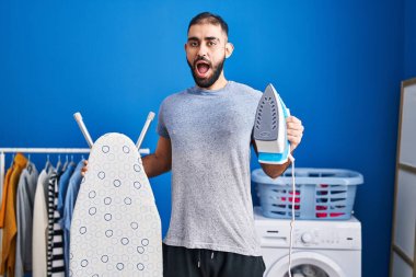 Elinde elektrikli ütü tutan Ortadoğu 'lu adam çılgınca kutlama yapıyor ve başarıya hayret ediyor gözleri açık heyecanla haykırıyor. 