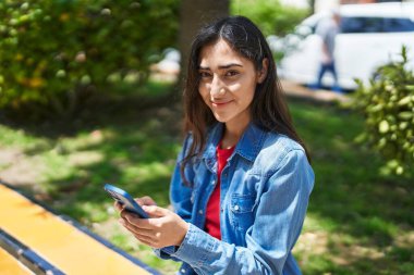 Young hispanic girl smiling confident using smartphone at park