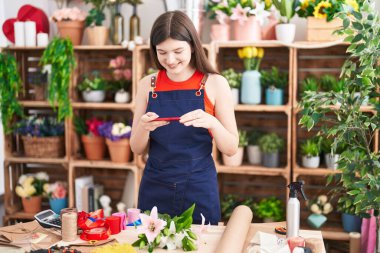 Young caucasian woman florist make photo by smartphone to flowers at florist