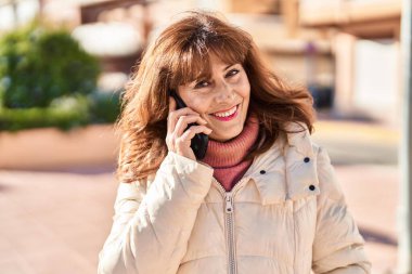 Orta yaşlı bir kadın gülümsüyor. Parktaki akıllı telefondan konuşuyor.