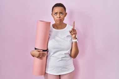 Güzel Afrikalı Amerikalı kadın yoga minderi tutuyor üzgün ve üzgün görünüyor, parmaklarıyla yön gösteriyor, mutsuz ve depresif.. 