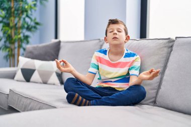 Sarışın çocuk evdeki kanepede yoga egzersizi yapıyor.