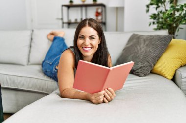 Evdeki kanepede uzanmış kitap okuyan güzel İspanyol kadın.