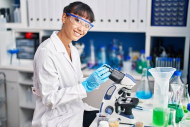 Young beautiful hispanic woman scientist smiling confident using microscope at laboratory