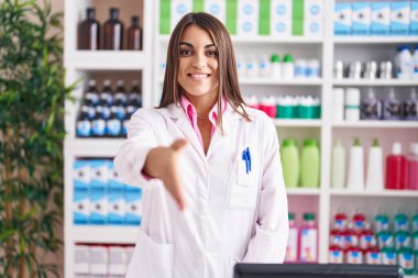 Young beautiful hispanic woman pharmacist smiling confident shake hand at pharmacy