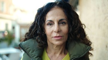 Middle age hispanic woman standing with relaxed expression at street