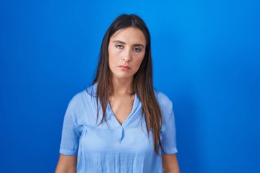 Young brunette woman standing over blue background looking sleepy and tired, exhausted for fatigue and hangover, lazy eyes in the morning. 