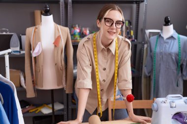 Genç beyaz kadın terzi atölyede kendine güvenerek gülümsüyor.