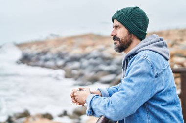 Genç kel bir adam, deniz kenarında ciddi bir ifadeyle Balustrade 'a yaslanıyor.