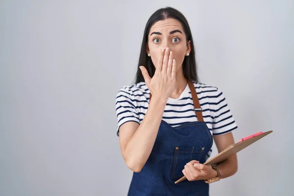 Young Brunette Woman Wearing Professional Waitress Apron Clipboard Covering Mouth — Stock Photo, Image