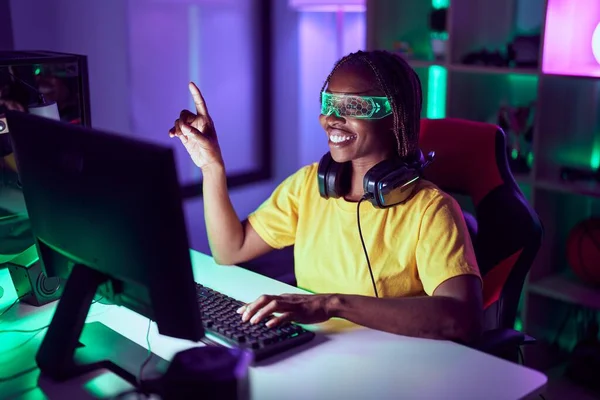 アフリカ系アメリカ人の女性のストリーマーは ゲームルームで仮想現実ガラスを使用してビデオゲームをプレイ — ストック写真
