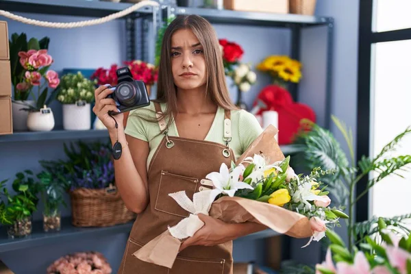 Mujer Morena Joven Que Trabaja Floristería Sosteniendo Cámara Escéptica Nerviosa —  Fotos de Stock