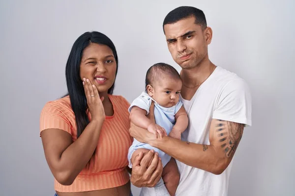 歯痛や歯の病気のために痛みを伴う表現で手で口に触れる孤立した背景の上に一緒に立って赤ちゃんを持つ若いヒスパニック系のカップル 歯科医のコンセプト — ストック写真