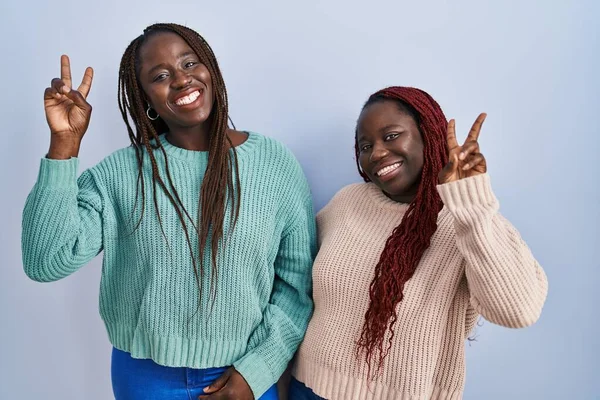 Две Африканки Стоят Синем Фоне Улыбаются Глядя Камеру Показывая Пальцы — стоковое фото