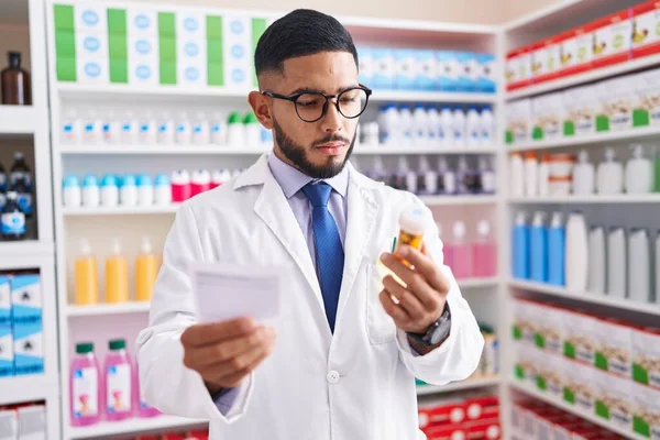 Young Latin Man Pharmacist Holding Pills Bottle Reading Prescription Pharmacy — Zdjęcie stockowe