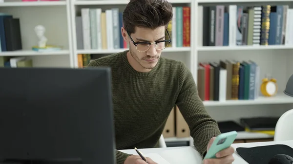 Young Hispanic Man Student Using Smartphone Writing Notebook Library University — Foto Stock