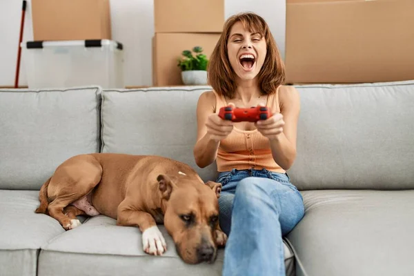 Young caucasian woman playing video game sitting on sofa with dog at home