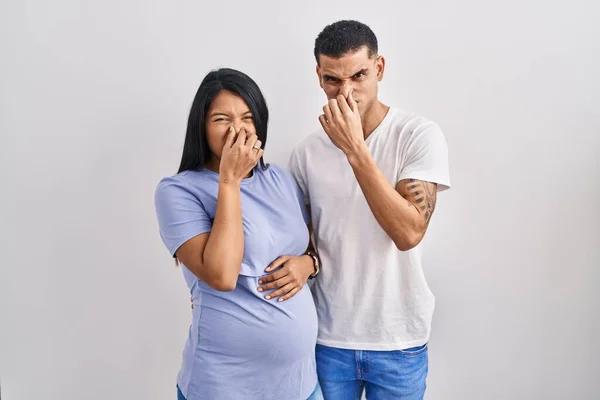 若いヒスパニック系のカップルは 赤ちゃんが鼻の上に指で息を保持し 臭いや嫌な 耐え難い匂いを嗅ぐ背景の上に立って期待しています 臭いが悪い — ストック写真