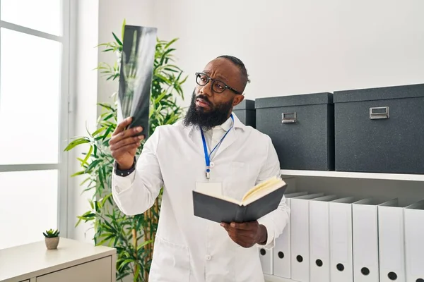 Joven Afroamericano Hombre Vistiendo Doctor Uniforme Lectura Libro Buscando Xray — Foto de Stock