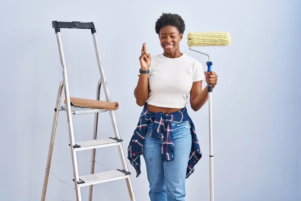 Mulher Afro Americana Segurando Rolo Pintor Gesto Dedo Cruzado Sorrindo — Fotografia de Stock