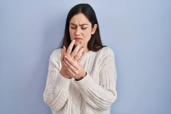 stock image Young brunette woman standing over blue background suffering pain on hands and fingers, arthritis inflammation 