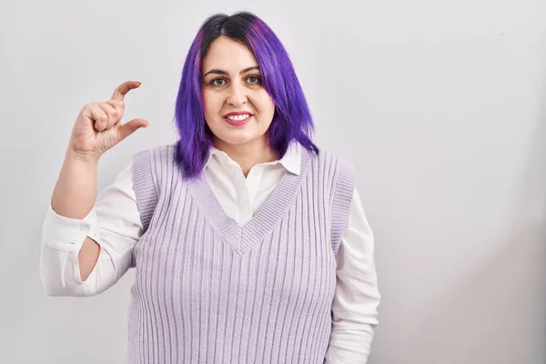 另外一个身材魁梧的女人站在白色背景的紫色头发上 微笑着 自信地做手势 手拿着小尺寸的标志 手拿着手指 手拿着相机 计量概念 — 图库照片