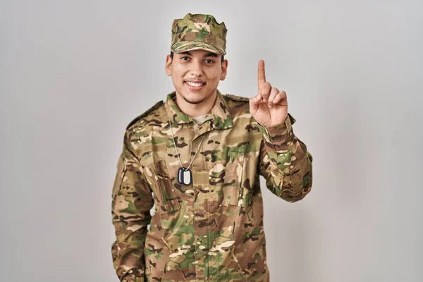 自信と幸せ笑顔ながら カモフラージュ軍の制服を着て指第1位を示すと指摘している若いアラブ人男性 — ストック写真