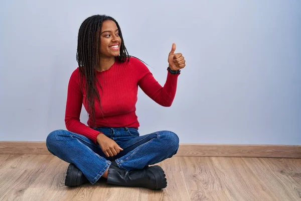 Joven Afroamericano Con Trenzas Sentado Suelo Casa Buscando Orgulloso Sonriendo —  Fotos de Stock