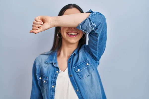 Hispanic Kvinne Står Blå Bakgrunn Dekker Øynene Med Armen Smilende – stockfoto