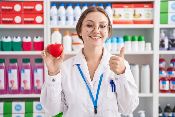 Молодая Белая Женщина Работающая Аптеке Держит Красное Сердце Улыбаясь Счастливым — стоковое фото