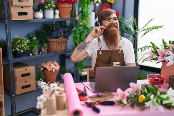 Young Redhead Man Florist Using Headset Laptop Working Flower Shop — Stok fotoğraf