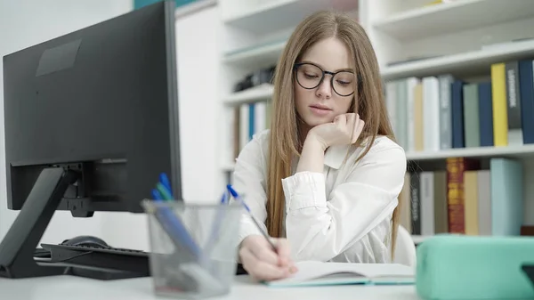 若いブロンドの女性の学生は 大学の教室でノートパソコンの書き込みを使用して — ストック写真