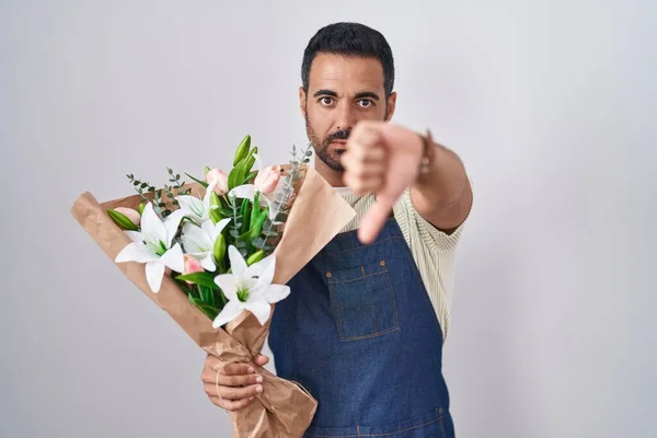Hispanic man with beard working as florist looking unhappy and angry showing rejection and negative with thumbs down gesture. bad expression.