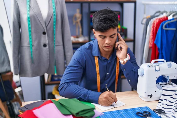 在服装厂 他的年轻人裁缝正在谈论在笔记本上写智能手机 — 图库照片